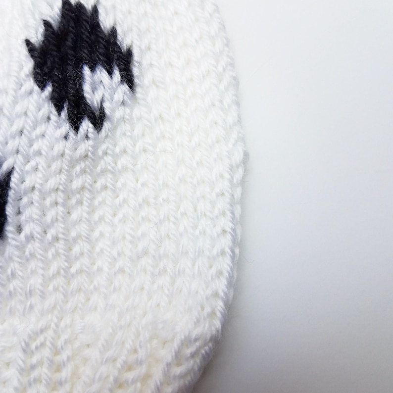 May include: White knitted hat with black and white polka dots. The hat is made of a soft, textured yarn.