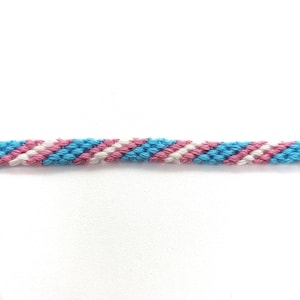 Puede incluir: Un brazalete de amistad azul, rosa y blanco con un patrón diagonal.
