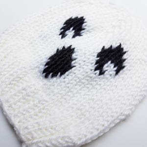 May include: White knitted hat with black embroidered eyes, resembling a ghost.