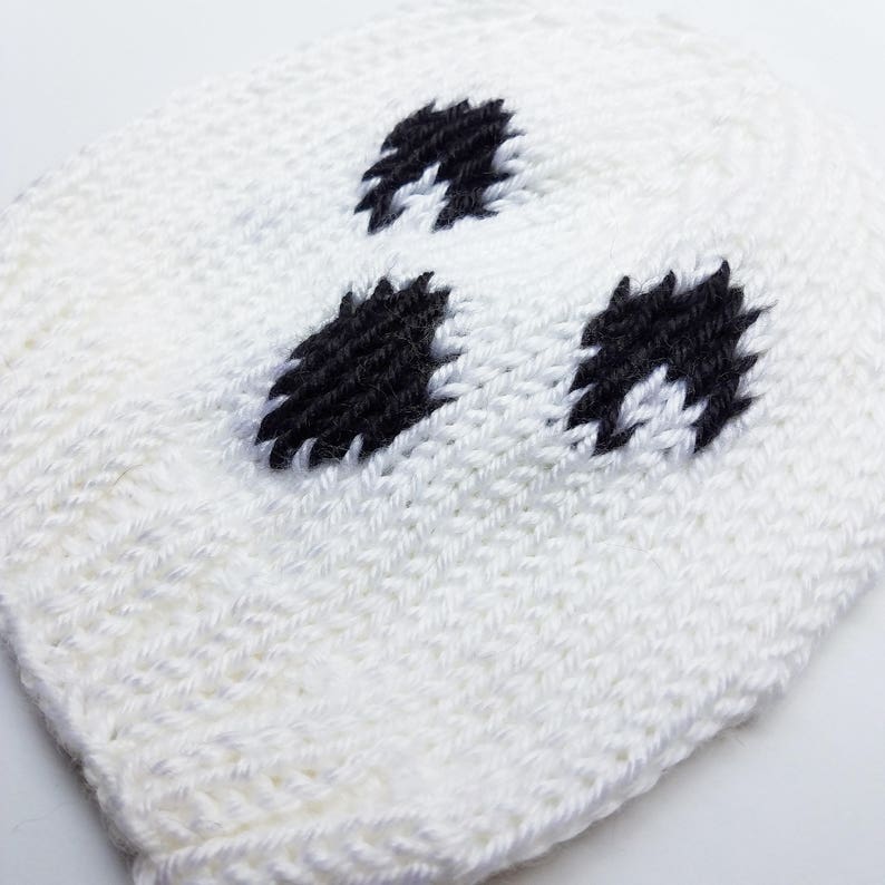 May include: White knitted hat with black embroidered eyes, resembling a ghost.