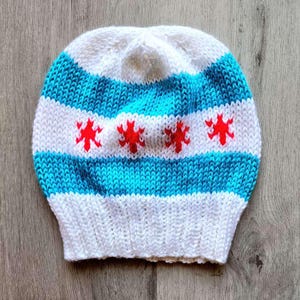 Könnte beinhalten: Eine gestrickte weiße und blaue Mütze mit roten Sternen. Die Mütze ist ein Chicago-Flaggen-Design.