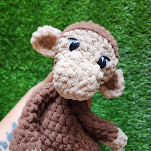 May include: A handmade crochet monkey in shades of brown and tan. The monkey has black eyes and a detailed face. The plush toy is soft and cuddly, perfect for children. The monkey's head and body are visible in the image.