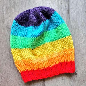 以下が含まれることがあります： 虹色のストライプのニットビーニー帽子。帽子は柔らかな糸で作られており、紫、青、緑、黄、オレンジ、赤など、さまざまな色があります。