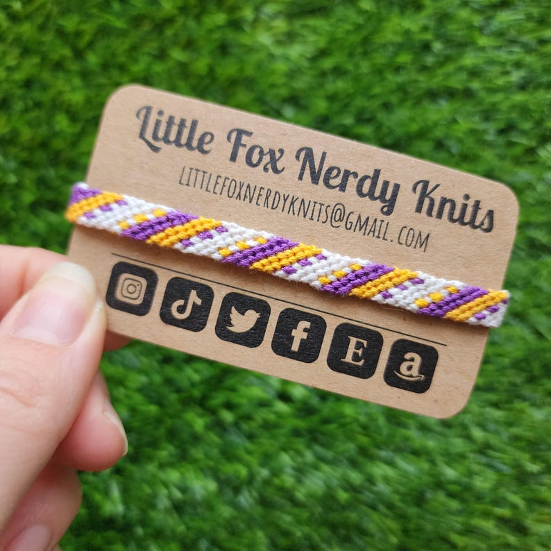 May include: A purple, yellow, and white friendship bracelet on a brown card with the text "Little Fox Nerdy Knits" and the email address "littlefoxnerdyknits@gmail.com". Social media icons are also included on the card.