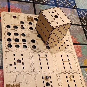 May include: A wooden puzzle cube with a laser-cut design. The cube is sitting on a wooden base with a grid pattern. The base has a QR code, the text "Puzzle Cube", and the text "Made in North Carolina".