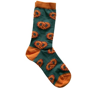 A pair of green socks patterned with orange salted pretzels has orange cuffs, heels and toes.