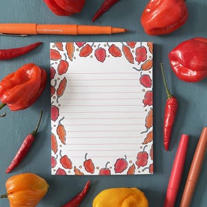 May include: A white notepad with a red, orange and yellow chilli pepper border. The notepad has lined paper and is ideal for jotting down notes or ideas.