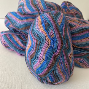 May include: A close-up of a ball of yarn with a multi-colored striped pattern in shades of blue, brown, pink, and beige. The yarn has a subtle sparkle.
