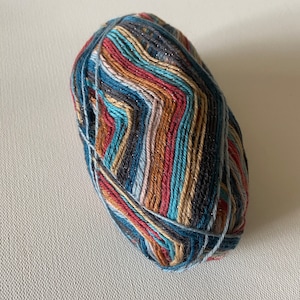 May include: A ball of colorful yarn with a multi-colored striped pattern and silver glitter. The yarn is wound into a ball shape and is ready for knitting or crocheting.