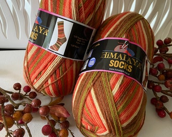 May include: Two skeins of Himalaya Socks yarn featuring a variegated color palette of orange, brown, cream, and olive green stripes. Each skein has a black paper label with the brand name, a graphic of a striped sock, and text including 437 yards.