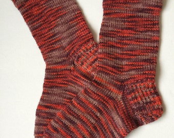 May include: A pair of hand-knitted socks in a striped pattern of brown, orange, and red.