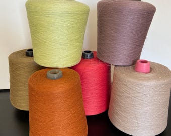 May include: A collection of six conical spools of yarn in various solid colors including lime green, muted brown, burnt orange, vibrant red, dusty mauve, and light beige. Each spool features a central plastic core and a textured thread surface.