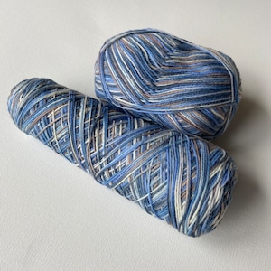 May include: Two skeins of blue, white, and brown yarn. One skein is rolled into a ball, and the other is a long skein.