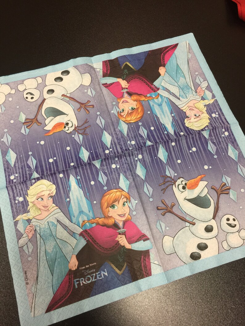 Puede incluir: Una servilleta de papel azul y morada con un dise&ntilde;o que presenta personajes de la pel&iacute;cula de Disney Frozen. Los personajes incluyen a Elsa, Anna y Olaf. El texto "From the movie" y "Disney's FROZEN" est&aacute; impreso en la servilleta.