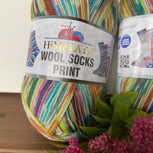 Puede incluir: Dos ovillos de lana de colores para tejer calcetines. La lana es una mezcla de rayas azules, verdes, rosas, naranjas y marrones. La etiqueta dice "Himalaya Wool Socks Print" e indica que la lana es lavable a máquina y secable en secadora. La lana tiene 437 yardas de largo.