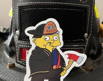 Puede incluir: Una pegatina con un personaje de dibujos animados amarillo vestido con un uniforme de bombero negro con rayas reflectantes amarillas, un casco con la etiqueta Fire E-1 Rescue y una hacha roja y plateada, sobre un casco de bombero negro.