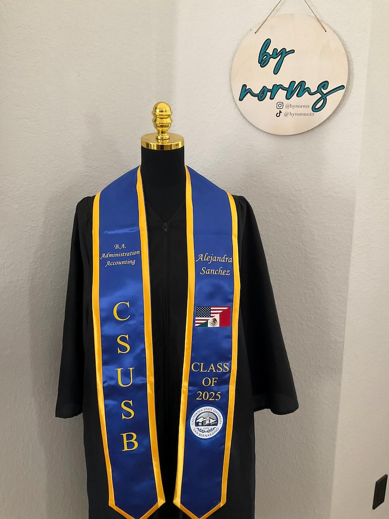 May include: A blue and gold graduation stole with the letters "CSUSB" and the text "B.A. Administration Accounting" and "Alejandra Sanchez". The stole also features a seal with the text "California State University San Bernardino" and "Class of 2025".