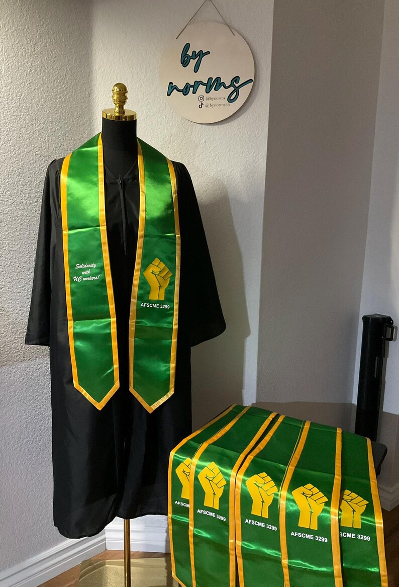 May include: Green and gold graduation sashes with a raised fist and the text "AFSCME 3299" and "Solidarity with UC workers!"