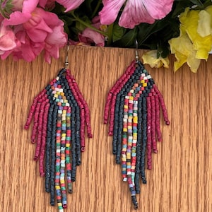 May include: A pair of long, beaded earrings with a geometric pattern. The earrings are made with red, black, and multi-coloured beads.