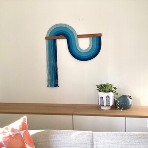 Puede incluir: Un tapiz de pared azul y blanco con una barra de madera, una planta en maceta y una figurita de p&aacute;jaro de cer&aacute;mica azul en un estante de madera.