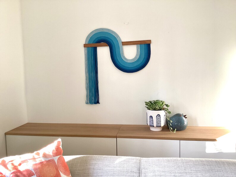Puede incluir: Un tapiz de pared azul y blanco con una barra de madera, una planta en maceta y una figurita de p&aacute;jaro de cer&aacute;mica azul en un estante de madera.