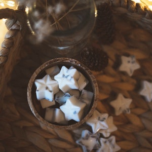 May include: A wooden bowl filled with white star-shaped wax melts, with a few more scattered around the bowl on a woven surface.