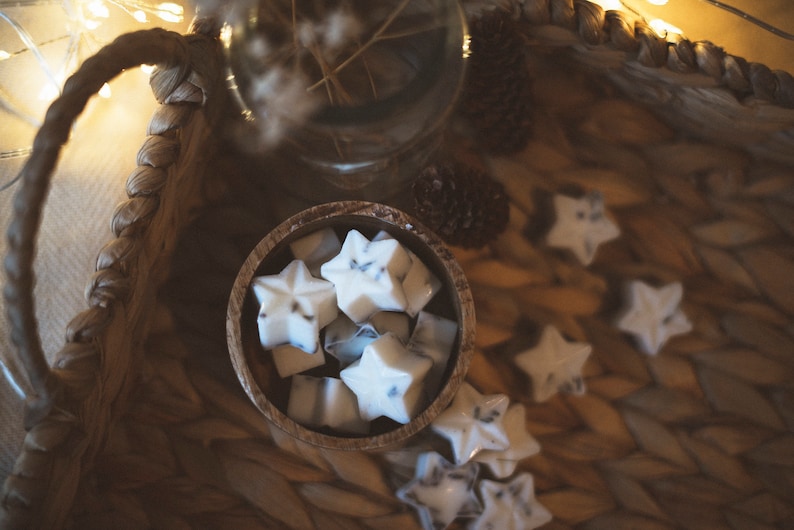 May include: A wooden bowl filled with white star-shaped wax melts, with a few more scattered around the bowl on a woven surface.