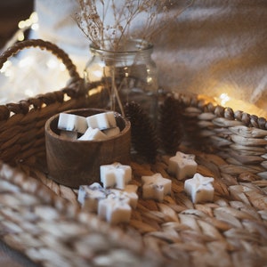 May include: A wicker basket filled with white star-shaped wax melts in a wooden bowl. The basket is on a white blanket with string lights.