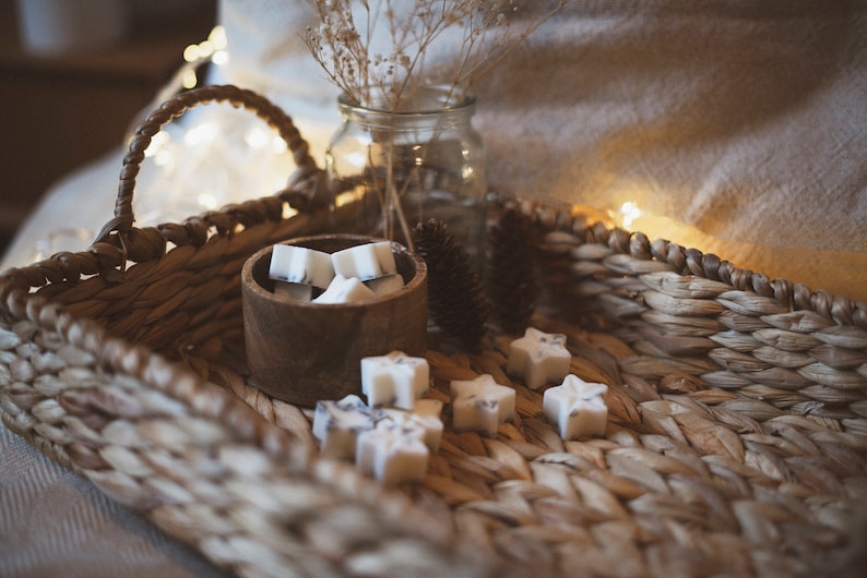 May include: A wicker basket filled with white star-shaped wax melts in a wooden bowl. The basket is on a white blanket with string lights.