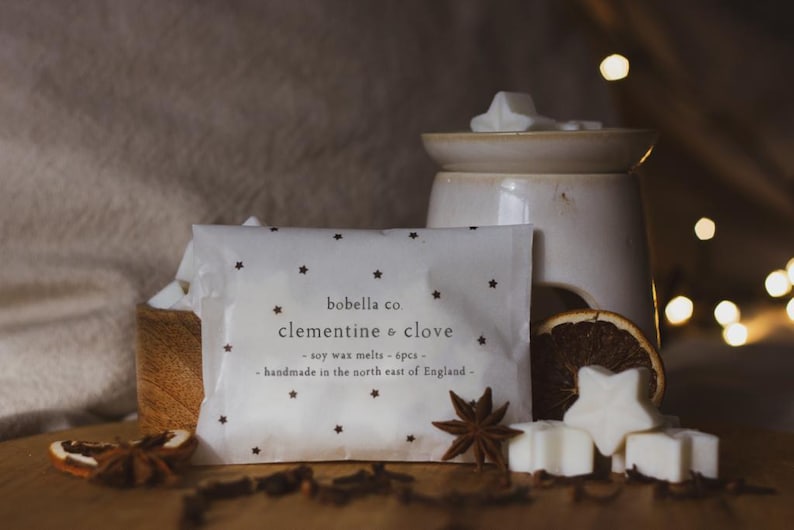May include: A white package with black stars printed on it. The package contains soy wax melts in the scent of clementine and clove. The text on the package reads "bobella co clementine & clove - soy wax melts - 6pcs - handmade in the north east of England - "