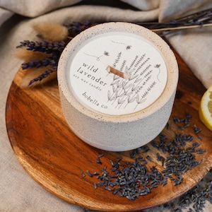 May include: A white concrete candle jar with a black and white illustration of lavender flowers and bees. The label reads "wild lavender soy wax candle bobella co."