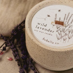 May include: A beige concrete candle jar with a white label that reads "wild lavender soy wax candle bobella co." The label features a line drawing of lavender flowers.