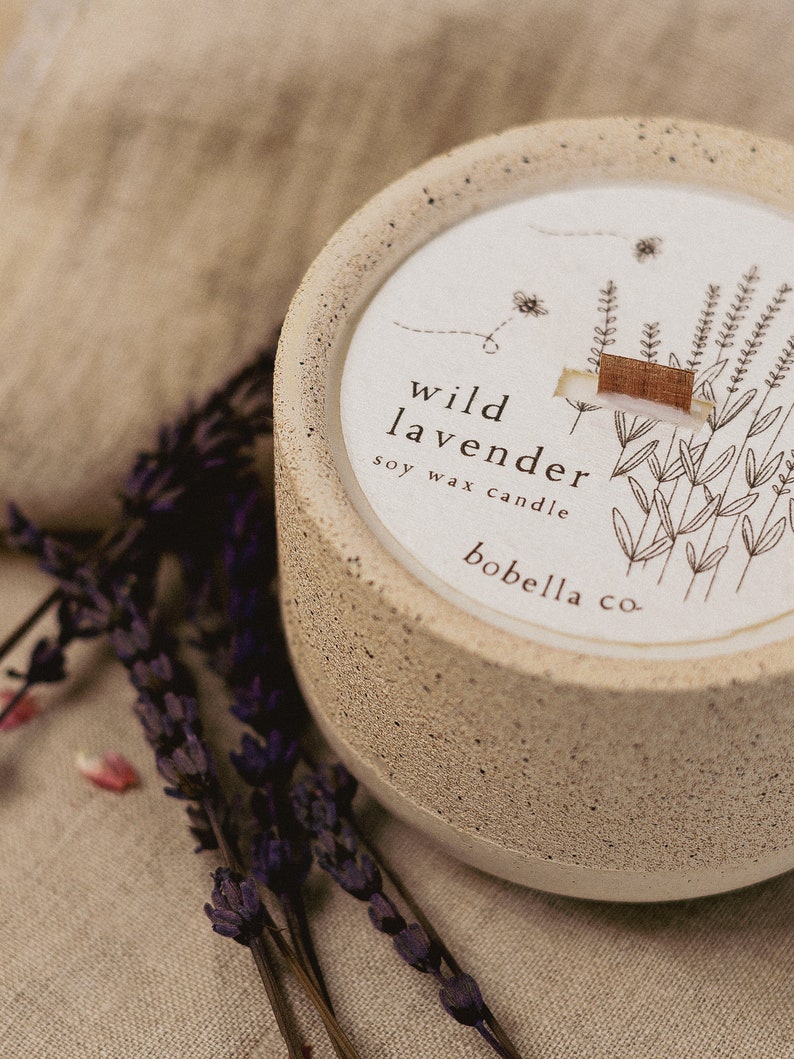 May include: A beige concrete candle jar with a white label that reads "wild lavender soy wax candle bobella co." The label features a line drawing of lavender flowers.