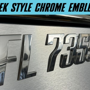 May include: Chrome license plate frame with the letters "FL" and the numbers "7359" in raised, reflective lettering.