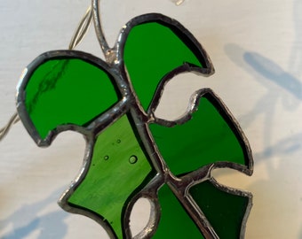 May include: A green stained glass leaf with a silver wire frame, hanging from a string of lights.