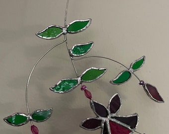 May include: A stained glass fuchsia flower mobile with green leaves and pink beads hanging from a silver wire.