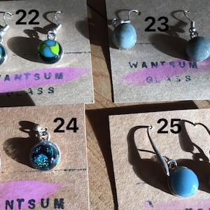 May include: A collection of handmade glass earrings. The earrings feature various designs, including a blue and green swirl, a speckled blue, and a blue sphere. The text "WANTSUM GLASS" is visible on the display cards. Each pair is numbered.