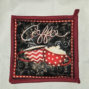 May include: Red and white quilted hot pad with a black background featuring two coffee mugs and the word "Coffee" in white cursive writing.