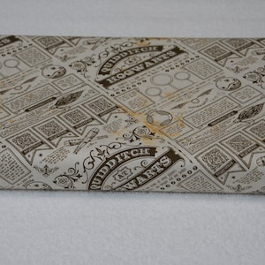 May include: A bolt of fabric featuring a repeating pattern of brown text and illustrations on a cream background. The design includes the words Quidditch at Hogwarts, along with drawings of brooms, balls, and various game-related icons.