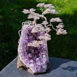 May include: A wire tree sculpture crafted from silver-toned wire, featuring intricate branches and foliage, mounted atop a natural amethyst geode with deep purple crystalline structures and a rough, earth-toned exterior rock base.