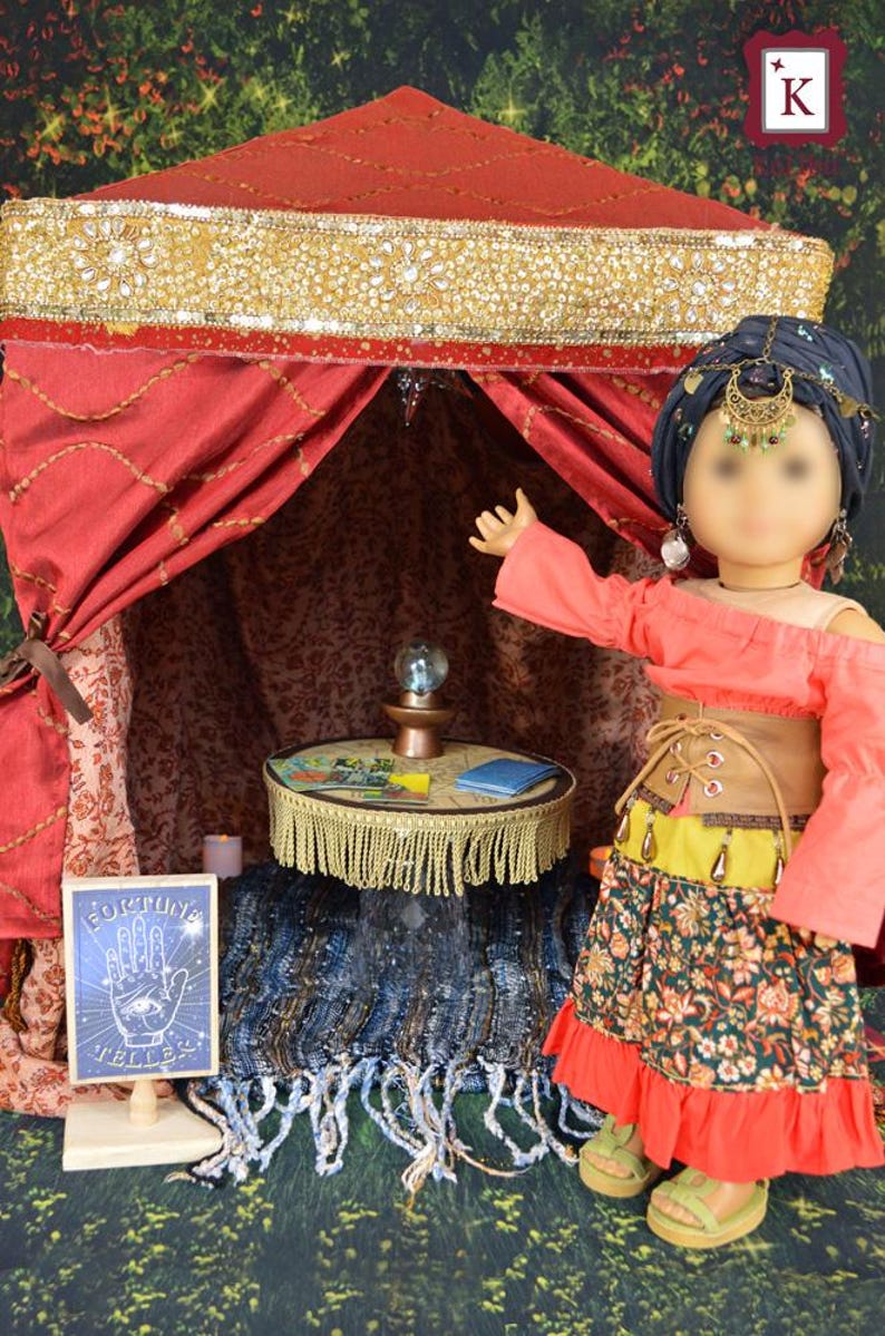 May include: A doll wearing a red and green outfit stands in a red tent with gold trim. The tent has a small table with a crystal ball and a sign that says "Fortune Teller".