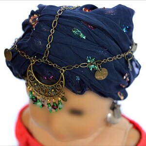 May include: A dark blue fabric head wrap with gold chain and coin accents. The chain has a crescent moon pendant with green and red beads hanging from it.