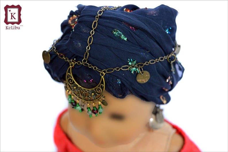 May include: A dark blue fabric head wrap with gold chain and coin accents. The chain has a crescent moon pendant with green and red beads hanging from it.