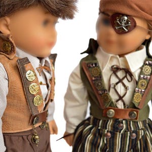 May include: Two dolls dressed in pirate costumes. One doll is wearing a brown vest with gold buttons and a brown hat. The other doll is wearing a green vest with gold accents and a brown bandana with an eye patch.