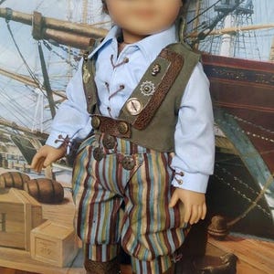 May include: A doll wearing a blue shirt, brown vest, striped pants, and brown boots. The doll has brown hair and is wearing an eye patch with a skull and crossbones design.