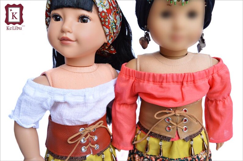 May include: Two dolls wearing off-the-shoulder tops and brown leather belts with laces. The doll on the left is wearing a white top and the doll on the right is wearing a coral top. Both dolls are wearing yellow skirts with beaded accents.