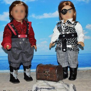 May include: Two dolls dressed as pirates, one with a red shirt and black vest, the other with a white shirt and black vest with skull and crossbones pattern. Both dolls are wearing grey pants and black boots. A wooden treasure chest is in the foreground.