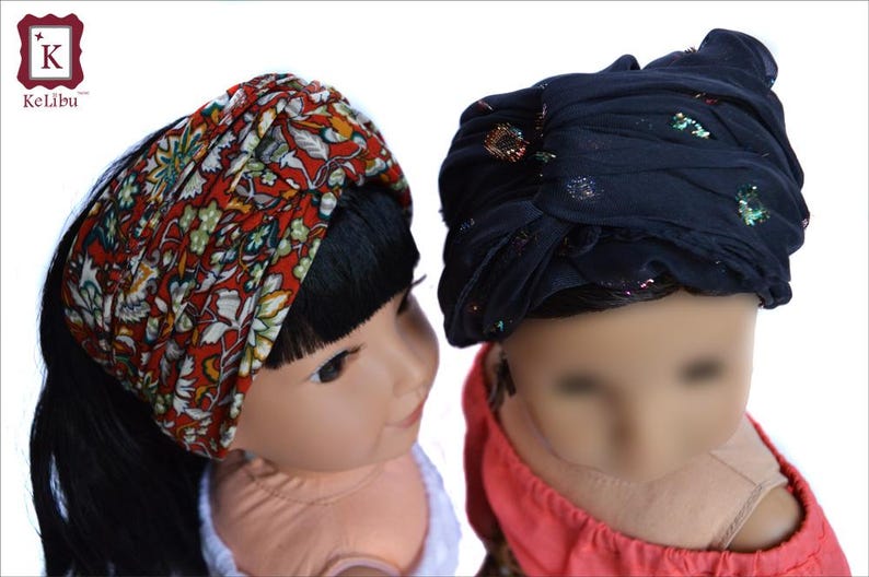 May include: Two dolls wearing headbands. One doll has black hair and is wearing a red and white floral headband. The other doll has brown hair and is wearing a dark blue headband with glitter.