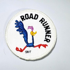 May include: Embroidered patch featuring the Road Runner cartoon character. The patch is circular with a white background and a blue, red, yellow, and pink Road Runner design. The words "ROAD RUNNER" are embroidered in black around the edge.