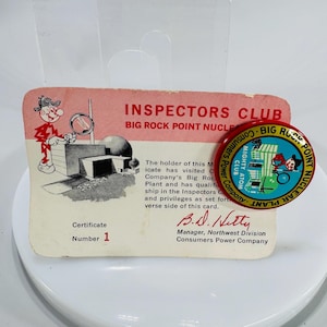 May include: Vintage Inspectors Club membership card and pin. The card is pink and white with a cartoon illustration and text. The pin is red, blue, and white, featuring a cartoon image and text. Both items are from Consumers Power Company.
